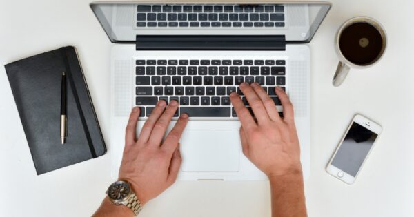 A man wearing a watch is typing on a laptop.